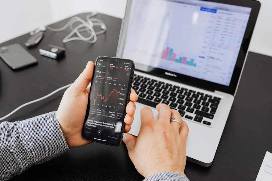 person checking stock market charts on phone and laptop